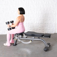 Thumbnail for Woman in pink activewear sitting on an adjustable weight bench, holding two dumbbells.