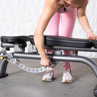 Thumbnail for Person in pink adjusting the backrest of a black and gray adjustable weight bench.