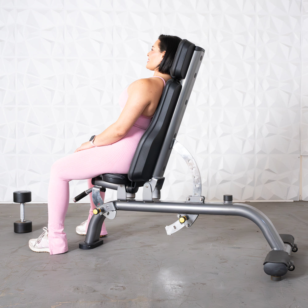 Woman in pink activewear sitting on an adjustable workout bench with a dumbbell on the floor.