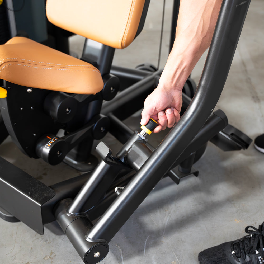 Hand adjusting the seat height on a black and tan chest press machine.