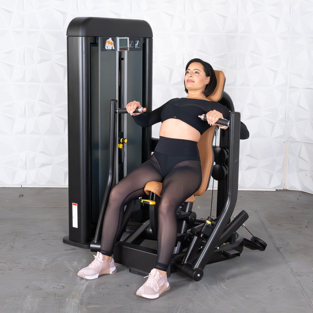 Woman in black activewear using a chest press machine with tan upholstery.