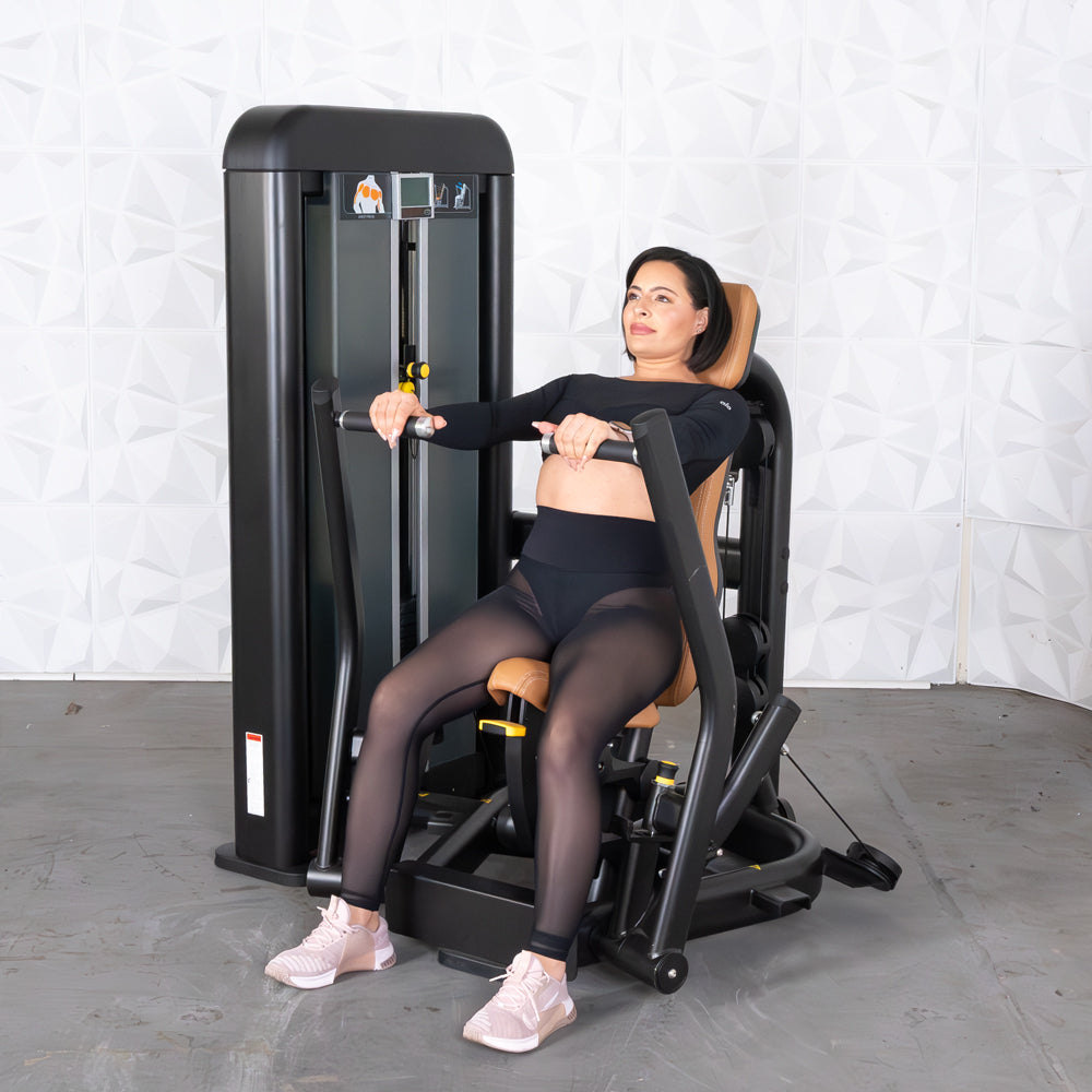 Woman using a black and tan chest press machine with a weight stack.