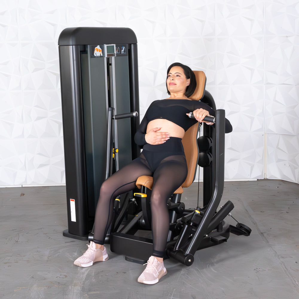 Woman in black workout clothes sitting on a commercial chest press machine with tan upholstery.