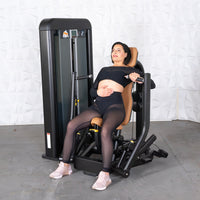 Thumbnail for Woman in black workout clothes sitting on a commercial chest press machine with tan upholstery.