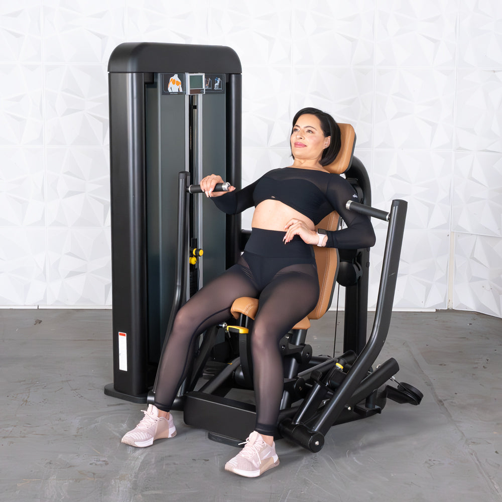 Woman in black activewear on a commercial chest press machine with tan upholstery.