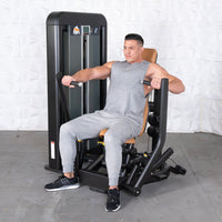 Thumbnail for Man in gray tank top and sweatpants using a black and brown chest press machine.