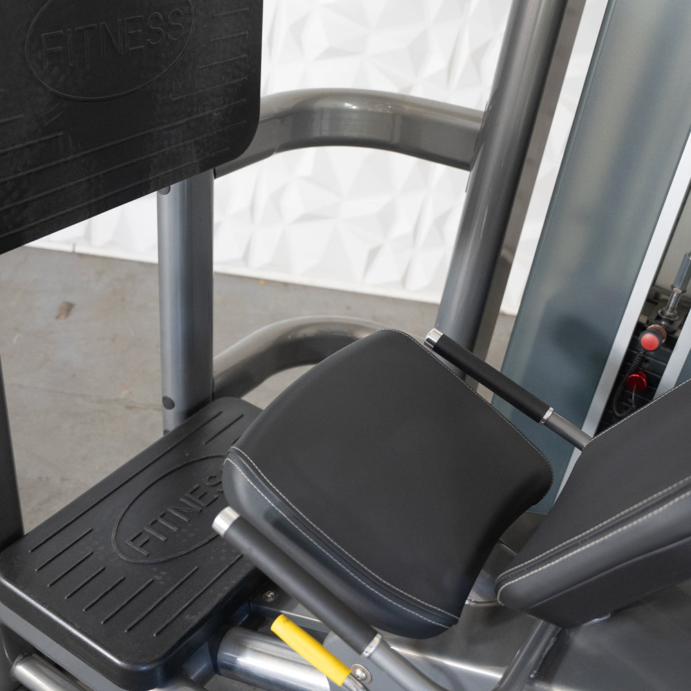 Close-up of a leg press machine with black footplates and padded seats, showing the "FITNESS" logo.