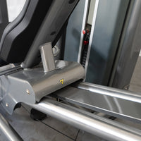 Thumbnail for Close-up of the leg press machine's seat and rails, showing a yellow warning triangle.