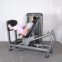 Thumbnail for Woman in pink pants and gray shirt using a gray leg press machine with black pads.