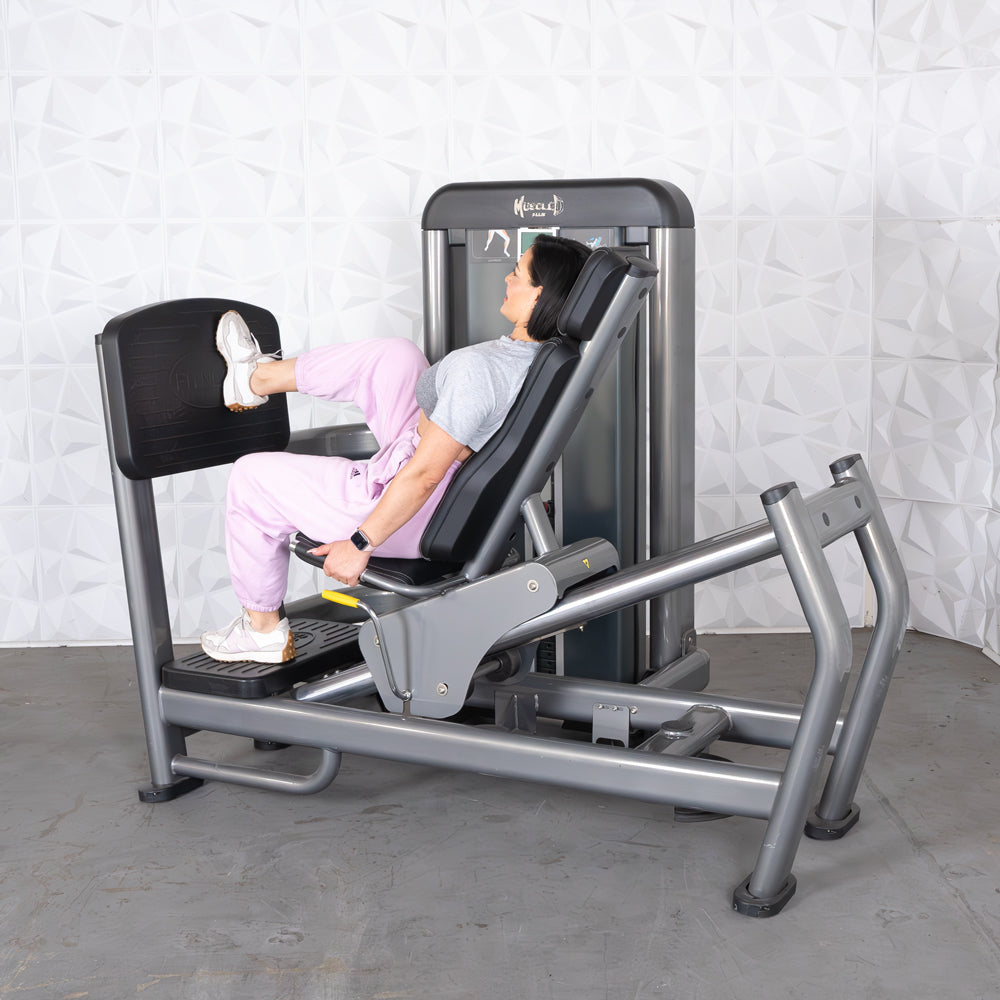 Woman using a gray leg press machine with a black footplate and seat.