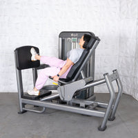 Thumbnail for Woman using a gray leg press machine with black pads, wearing pink pants and white sneakers.