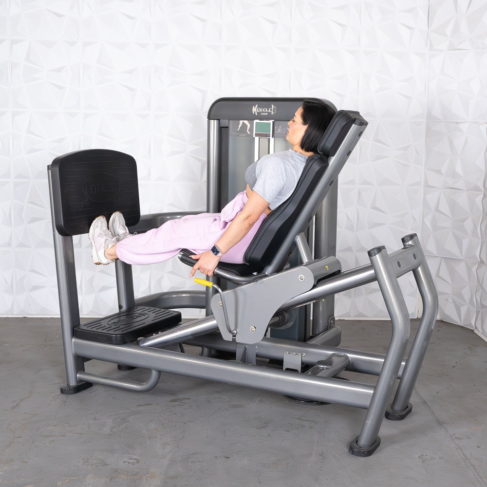 Woman using a gray leg press machine with black padding, pushing the footplate with her feet.