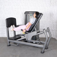 Thumbnail for Woman using a gray leg press machine with black padding, pushing the footplate with her feet.