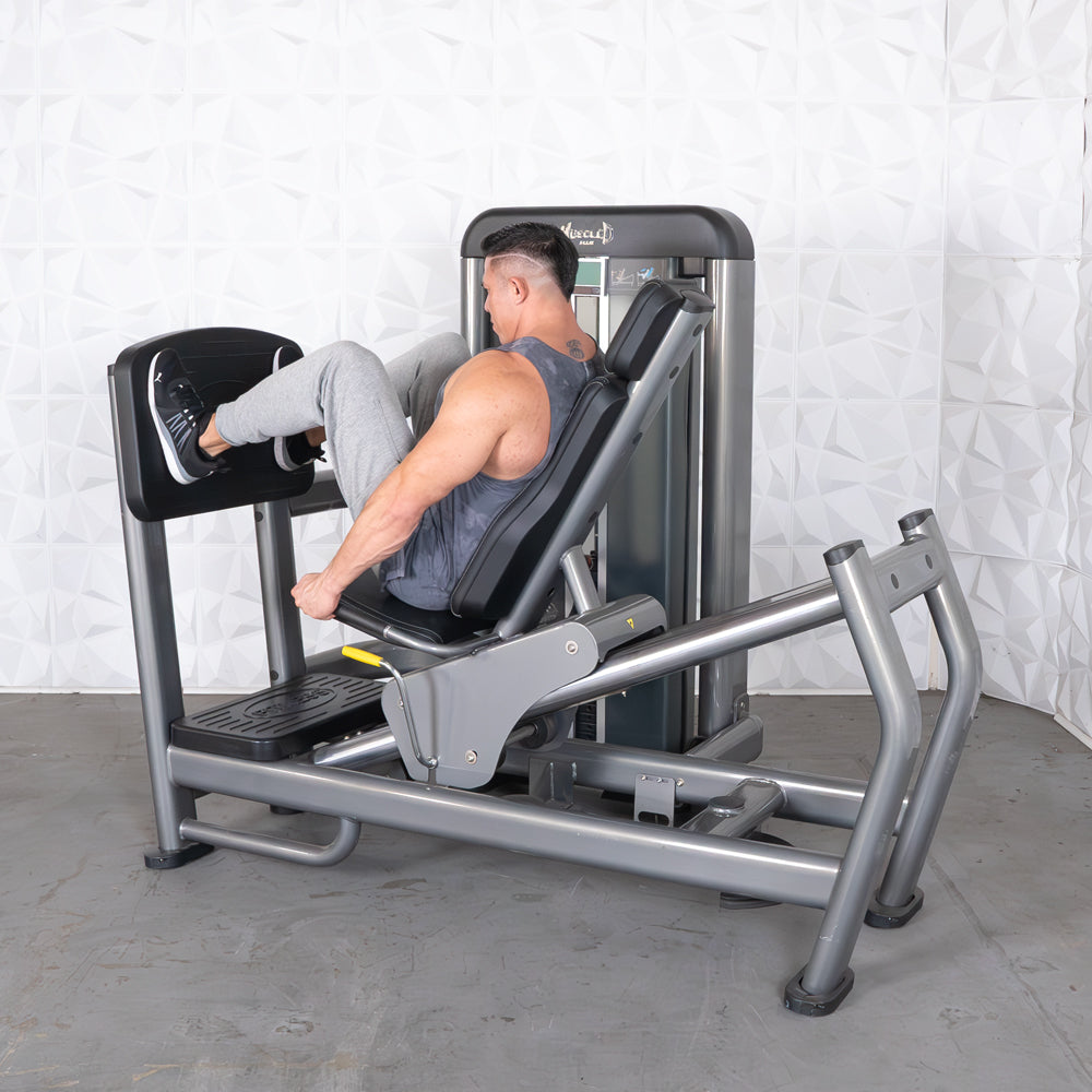 Man using a gray leg press and calf raise machine with black pads in a gym.