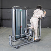 Thumbnail for Woman using a grey glute blaster machine in a gym, pushing back with one leg.