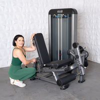 Thumbnail for Woman in green workout clothes next to a leg extension curl combo machine.