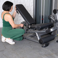 Thumbnail for Woman in green adjusting the seat of a gray leg extension curl combo machine.
