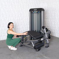 Thumbnail for Woman in green adjusting a gray leg extension curl combo machine.