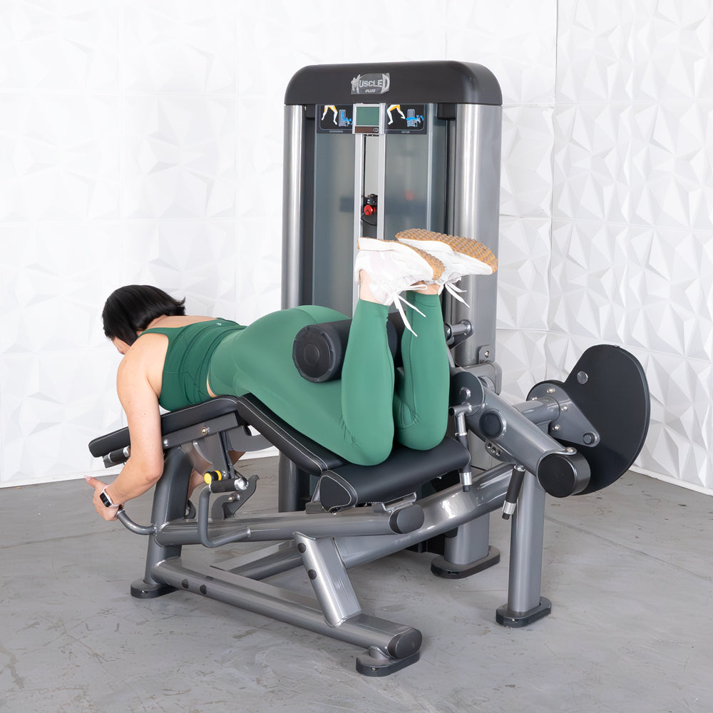 Woman in green using a leg extension curl combo machine, performing a leg curl.