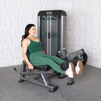 Thumbnail for Woman in green activewear using a leg extension curl machine, with a weight stack in the background.