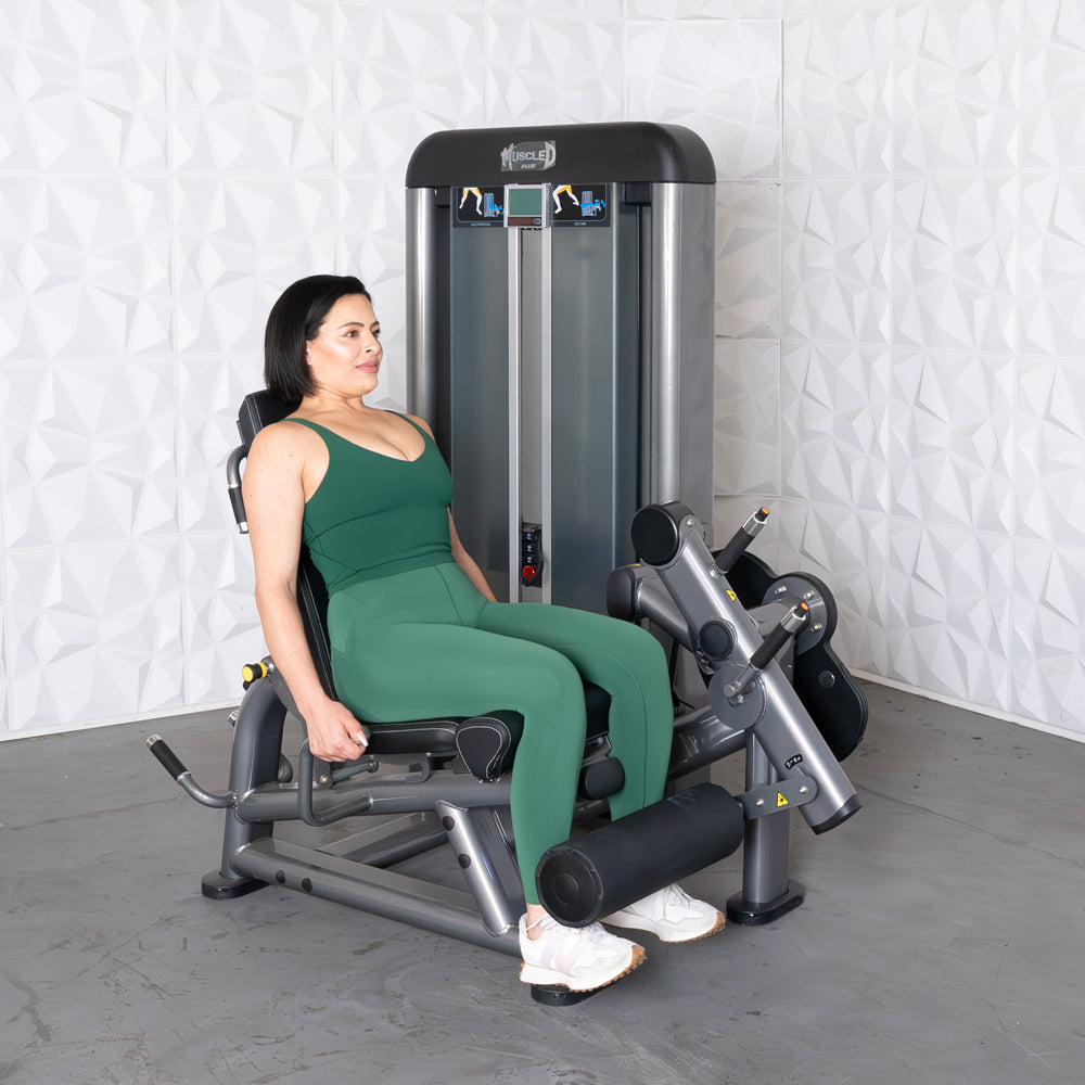 Woman in green using a leg extension curl combo machine.