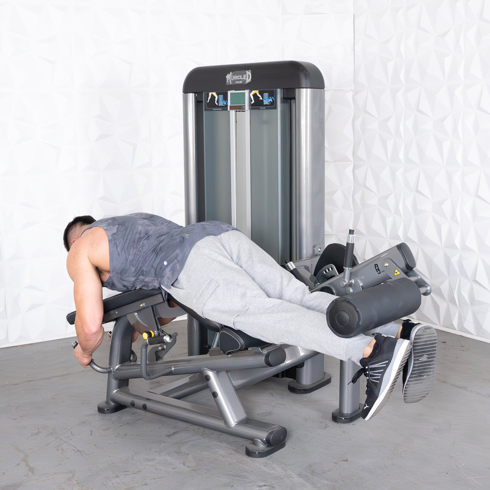 Man performing leg curls on a gray and black fitness machine.