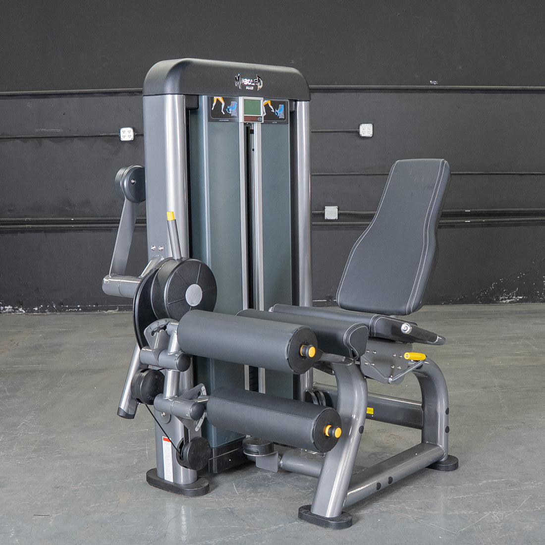 Gray leg extension curl combo machine with black padded seat and rollers on a concrete floor.