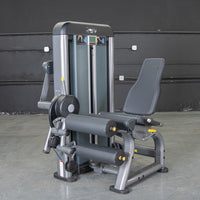 Thumbnail for Gray leg extension curl combo machine with black padded seat and rollers on a concrete floor.