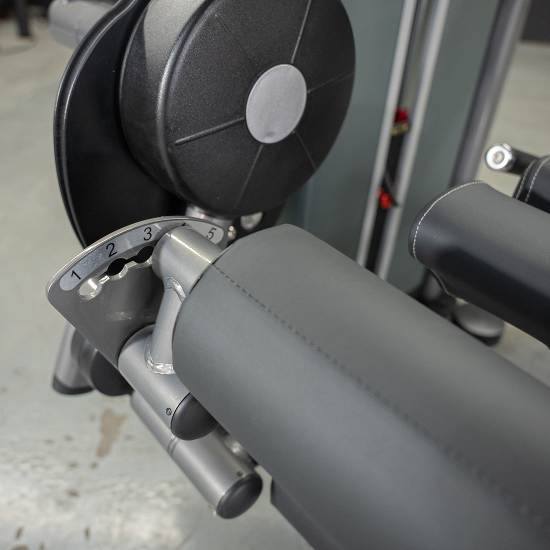 Close-up of a leg extension curl machine's adjustable padded roller and numbered setting dial.