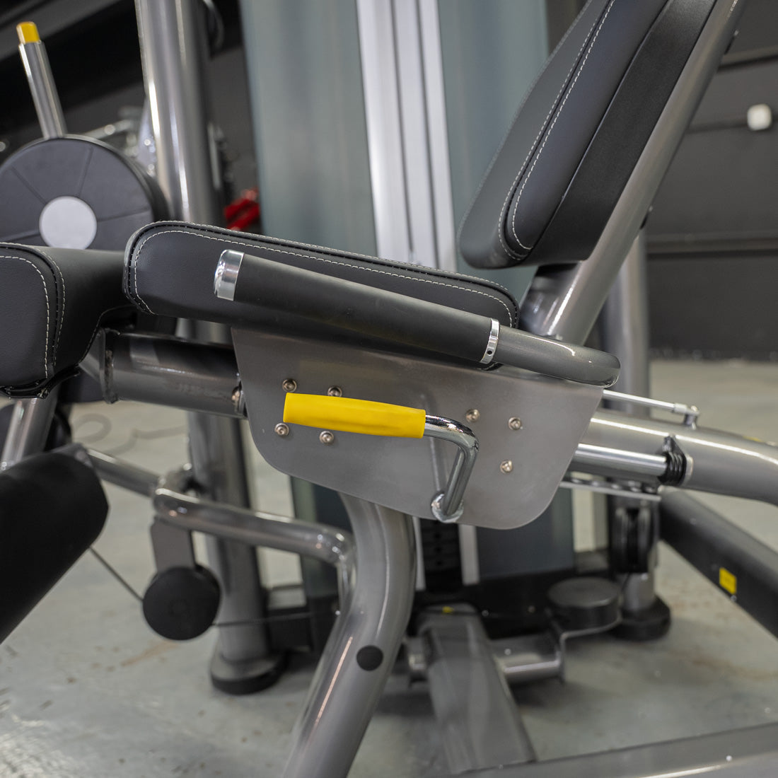 Close-up of a leg extension curl machine with black padded seats and a yellow adjustment handle.