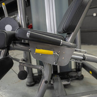 Thumbnail for Close-up of a leg extension curl machine with black padded seats and a yellow adjustment handle.