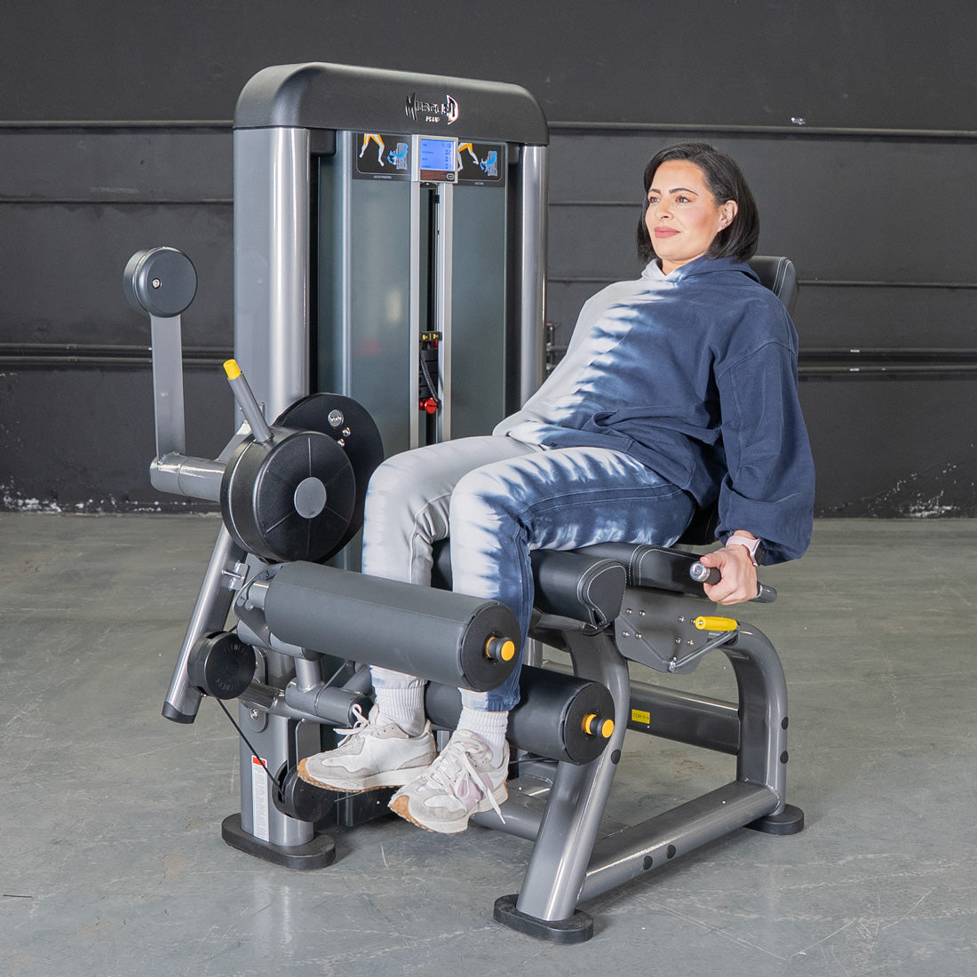 Woman using a gray and black leg extension curl machine in a gym.