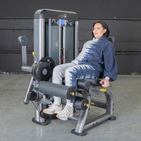 Thumbnail for Woman using a gray and black leg extension curl machine in a gym.