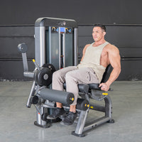Thumbnail for Man sitting on a gray leg extension curl combo machine, ready to exercise.