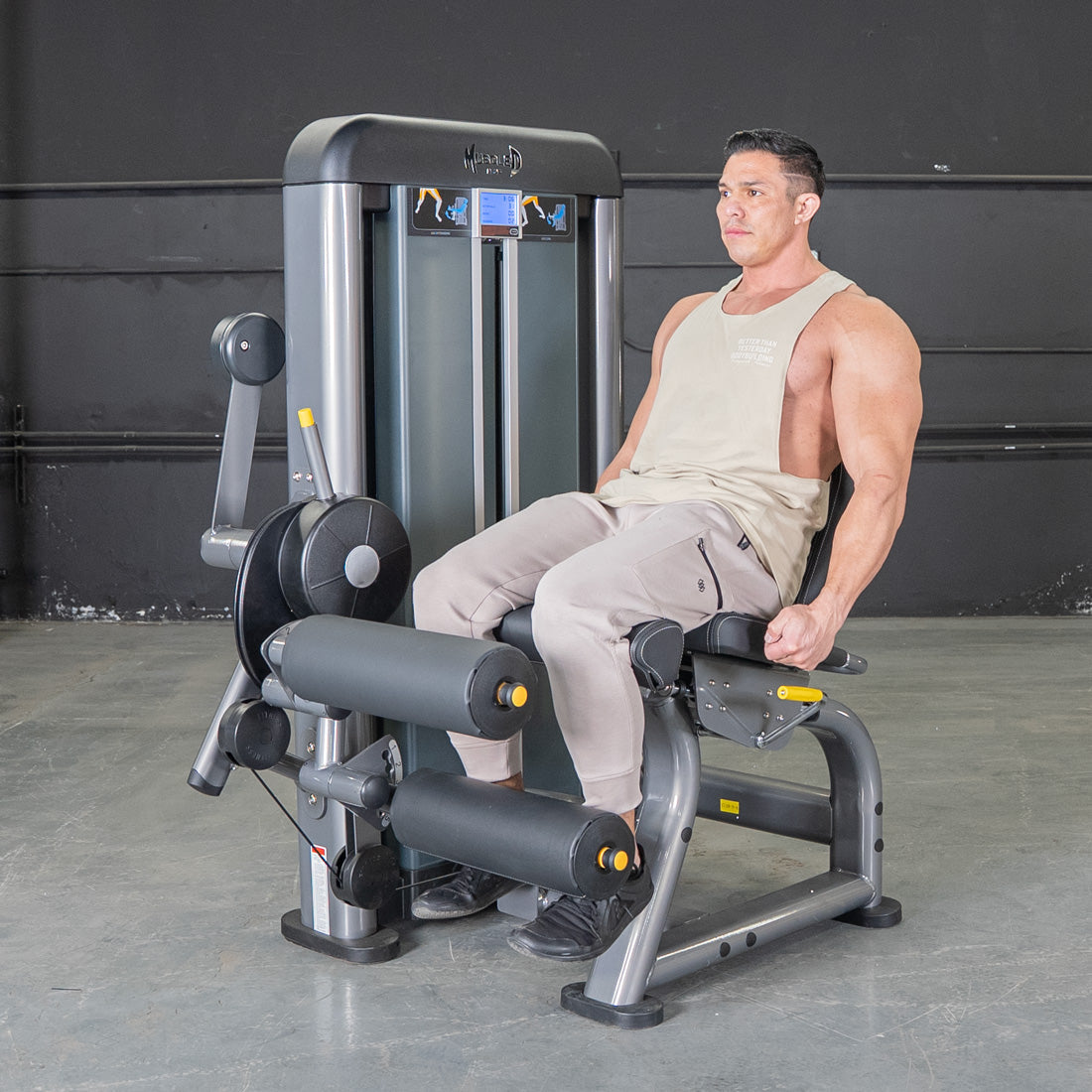 Man using a grey leg extension and curl combo machine with black padding and yellow accents.