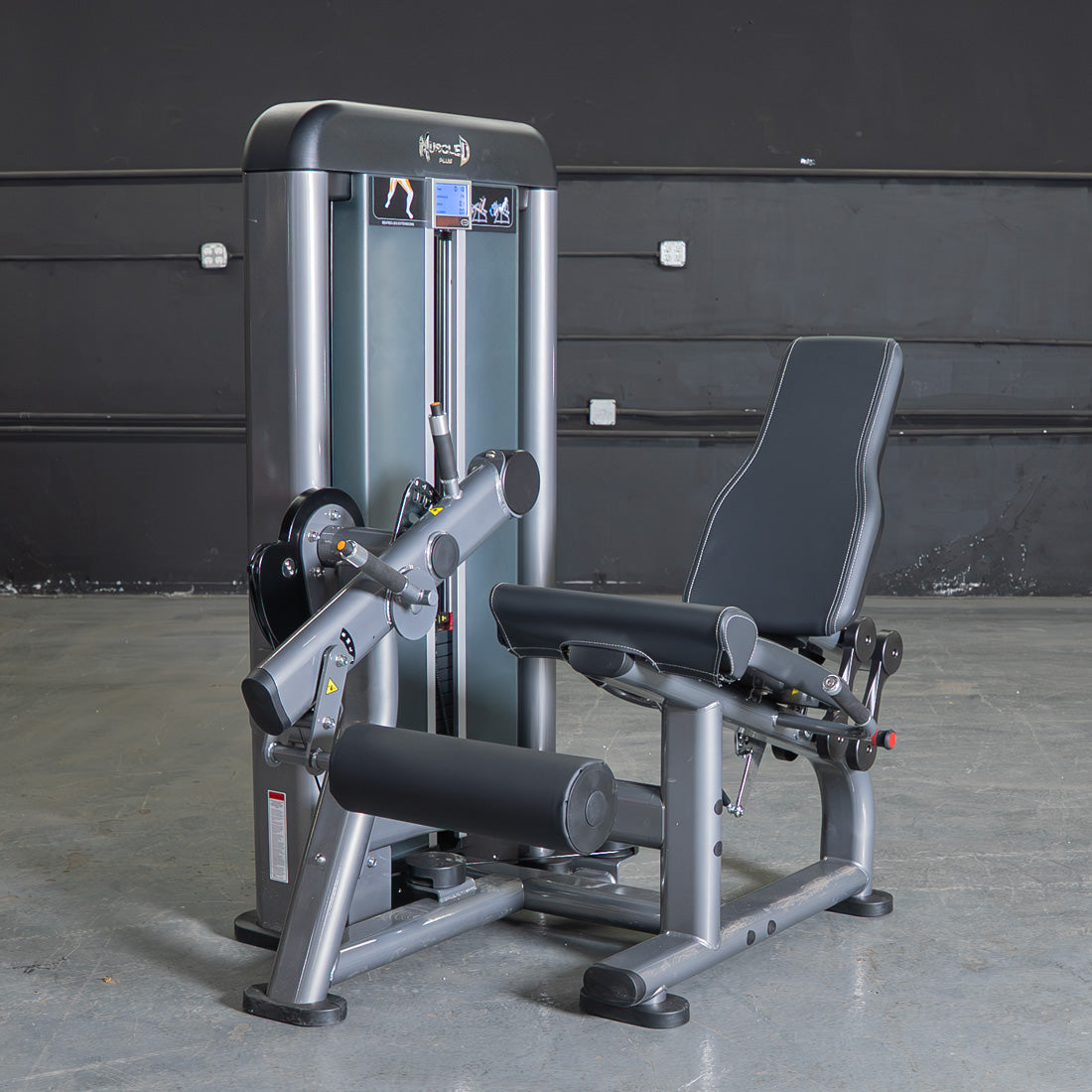 Gray and black leg extension machine with padded seat and rollers on a concrete floor.