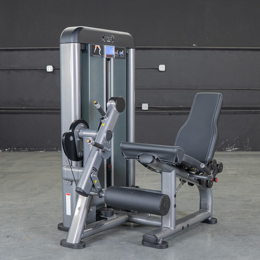 Gray and black leg extension machine with padded seat and rollers on a concrete floor.