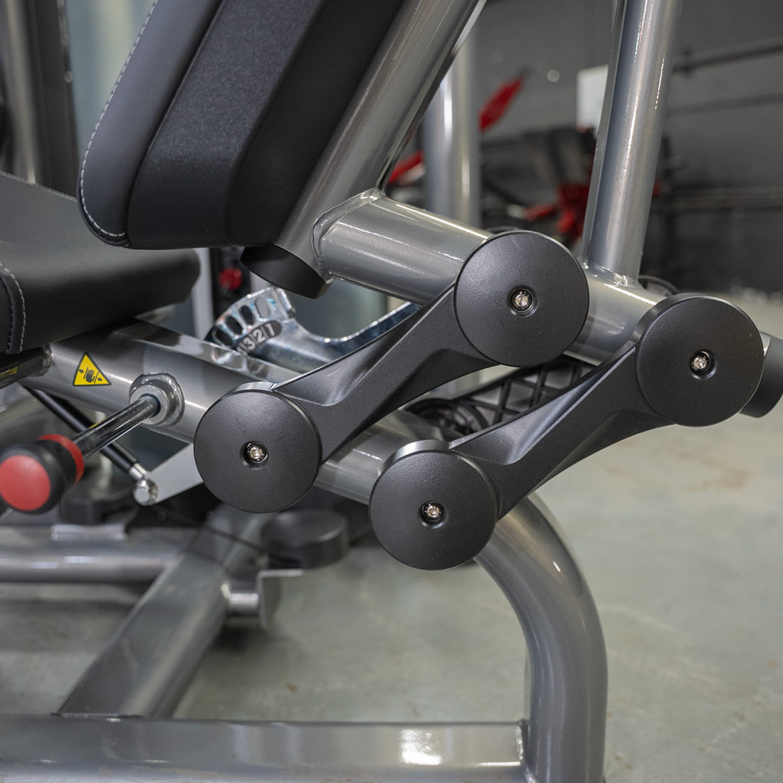 Close-up of the leg pads and adjustment mechanism on a silver leg extension machine.