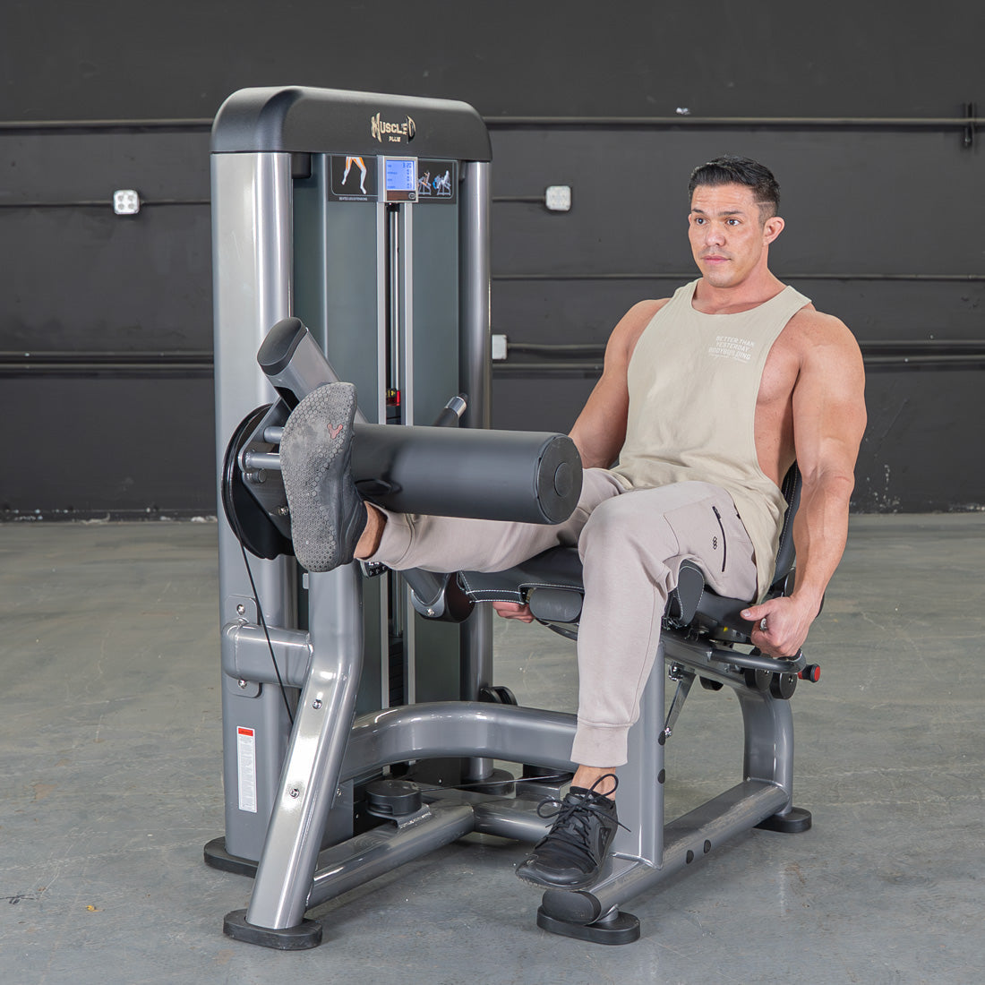 Man using a gray leg extension machine in a gym.