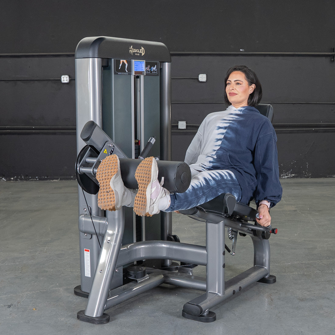 Woman using a gray leg extension machine, extending her legs forward.