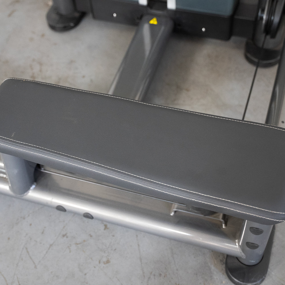 Close-up of a gray padded seat with white stitching on a silver metal frame of a fitness machine.