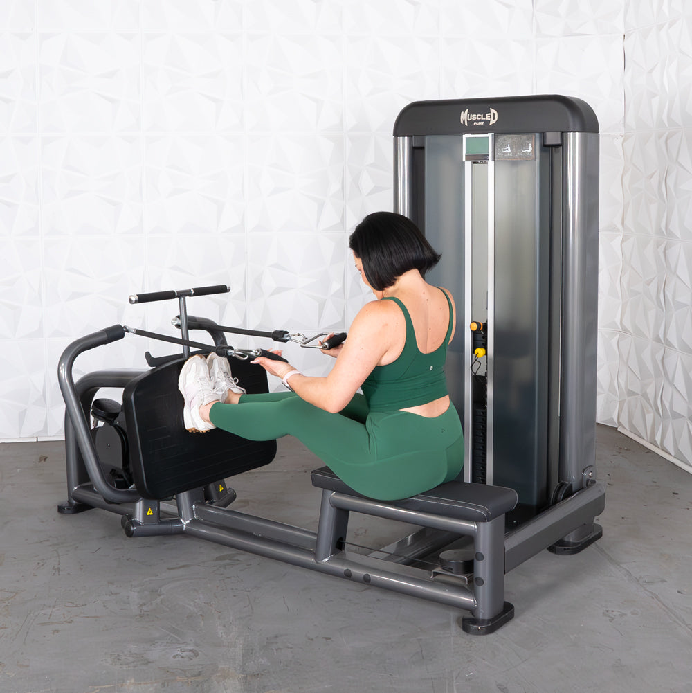 Woman in green activewear using a long pull row machine with feet on the footrest and hands on the handles.