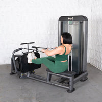 Thumbnail for Woman in green activewear using a gray long pull row machine with a white textured wall background.