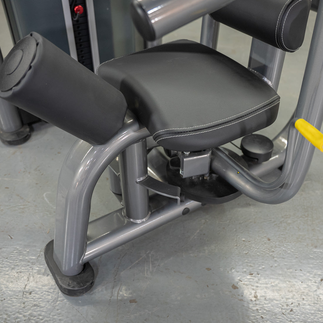 Close-up of a rotary torso machine's black padded seat and leg rests on a gray frame.