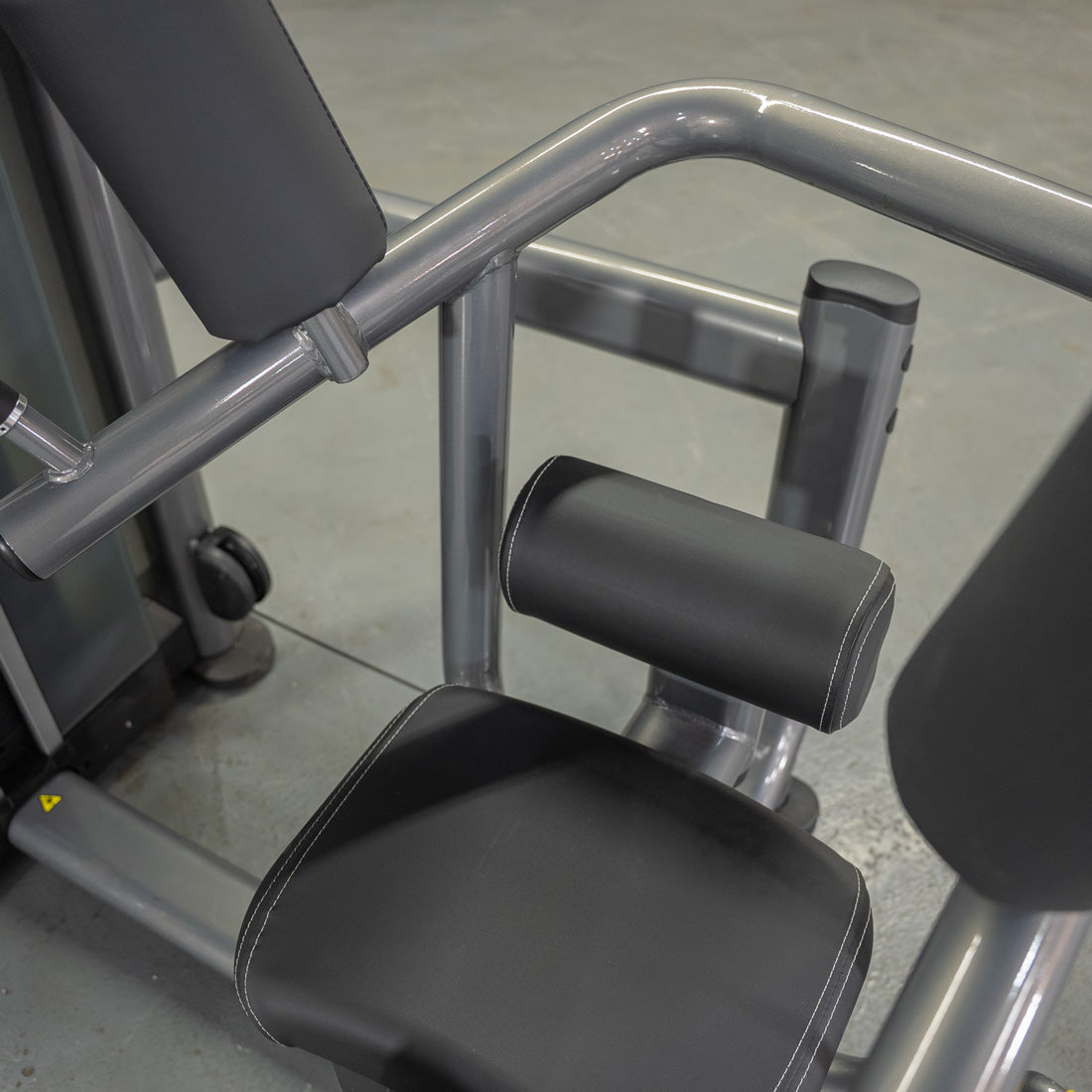 Close-up of a rotary torso machine with black padded seat and backrest, and gray metal frame.
