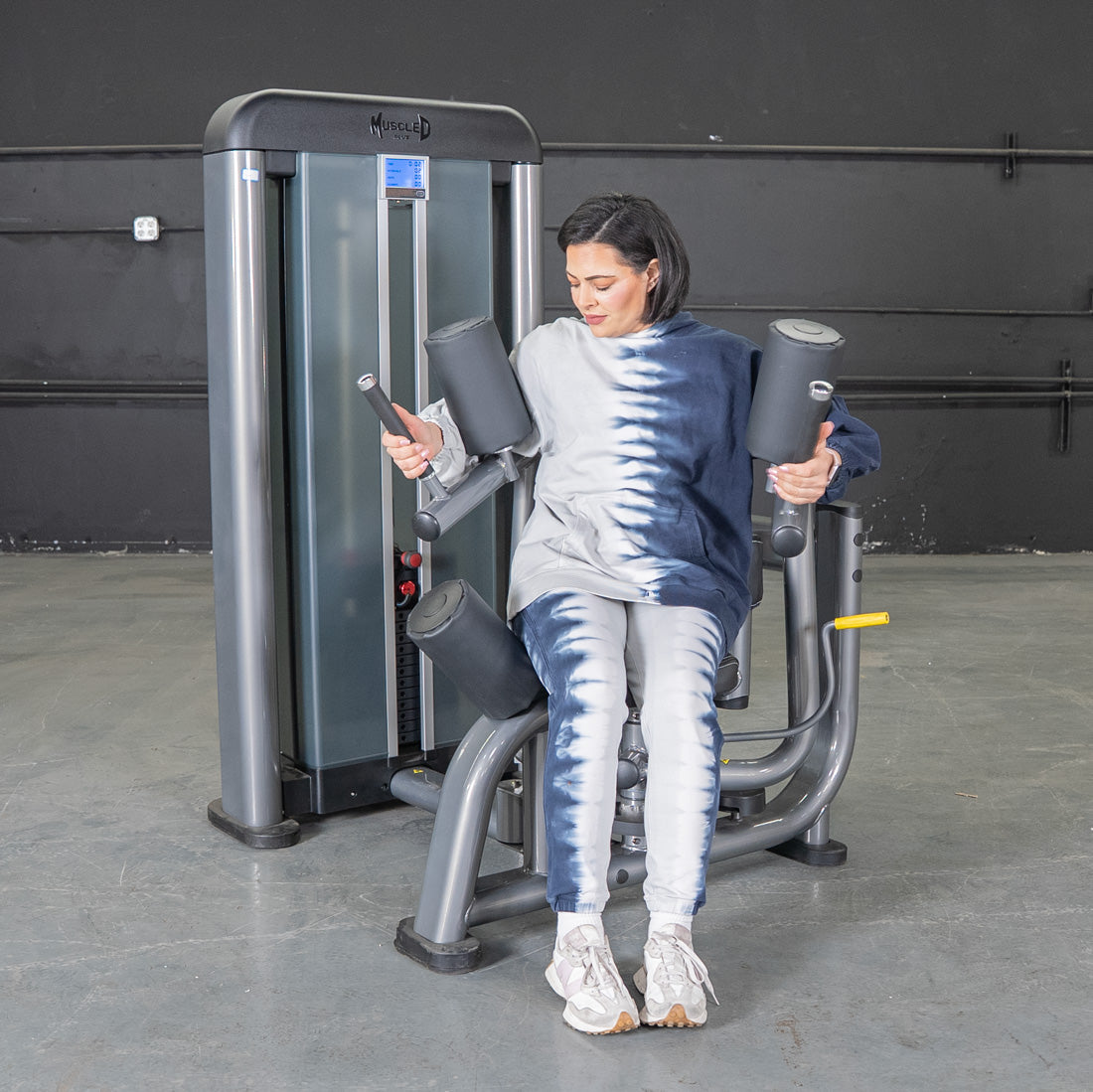 Woman in tie-dye using a gray rotary torso machine for obliques workout.