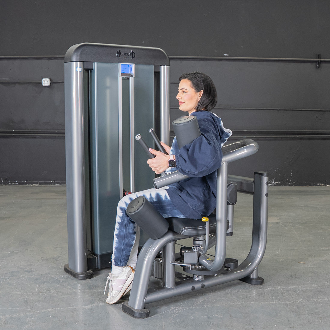 Woman in blue hoodie and tie-dye pants using a gray rotary torso machine.