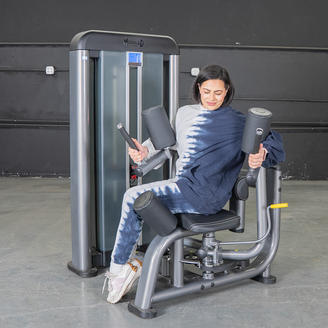 Woman using a gray rotary torso machine with black pads and a weight stack.
