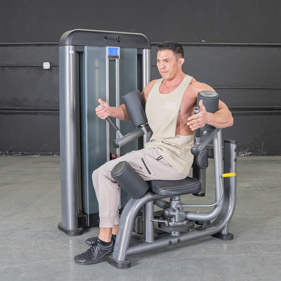 Man using a gray rotary torso machine with black padding in a gym.