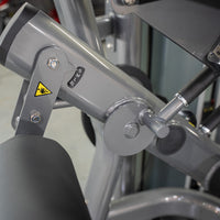 Thumbnail for Close-up of a leg curl machine's gray frame with S, M, L, XL size adjustments and a warning label.